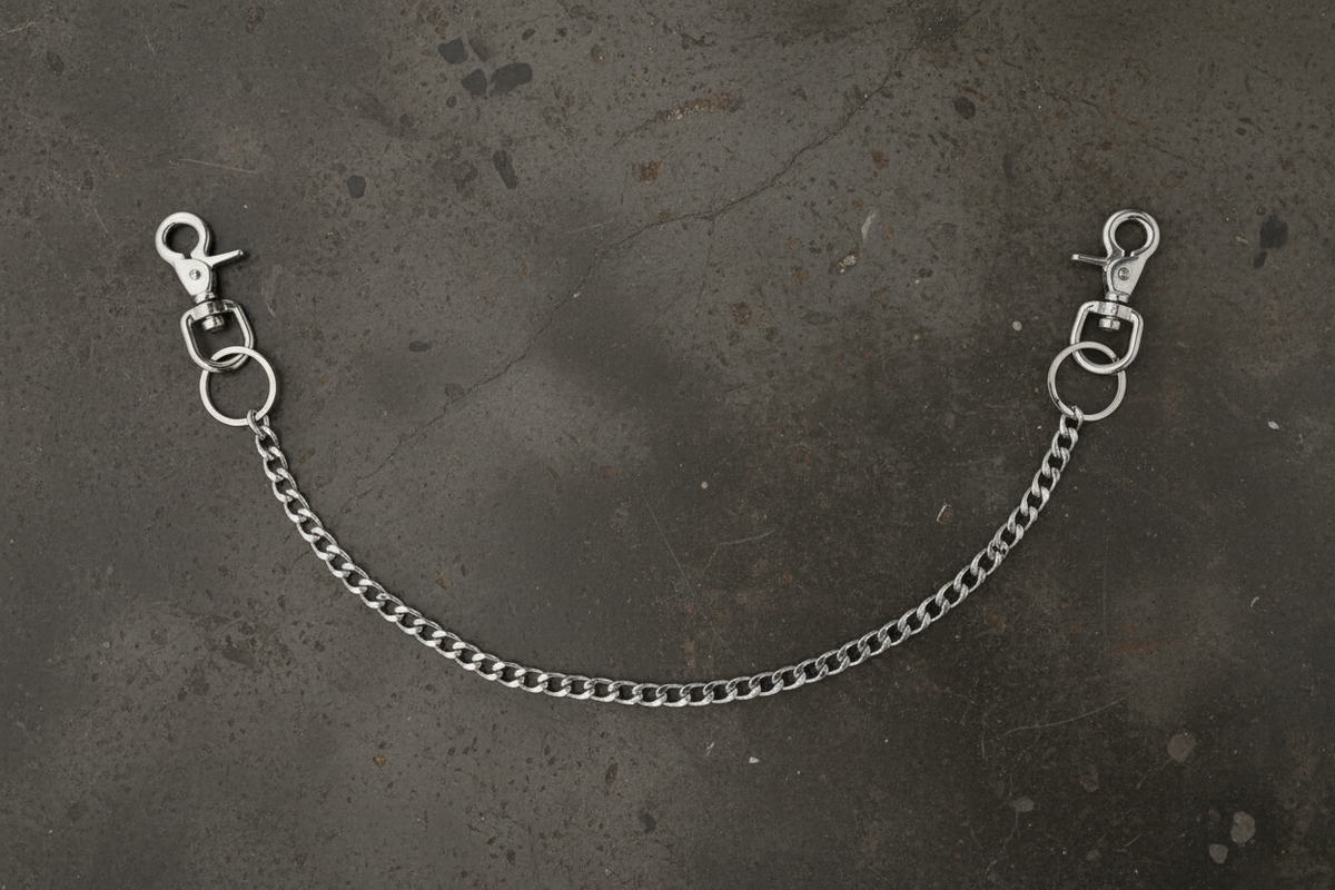 A silver metal chain extender with two lobster claw clamps and O-rings, laid out on a dark textured surface.