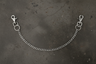 A silver metal chain extender with two lobster claw clamps and O-rings, laid out on a dark textured surface.
